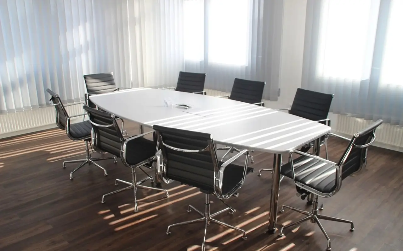 A bright, empty meeting room with a white table and black chairs