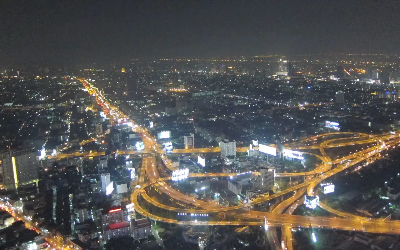 Bangkok at night, seen from above, with expressways of light running through the city
