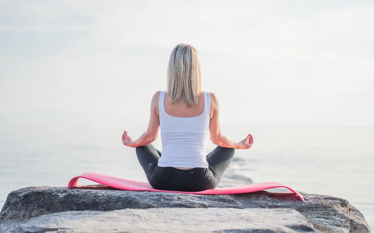 A woman meditating on a rock beside the sea